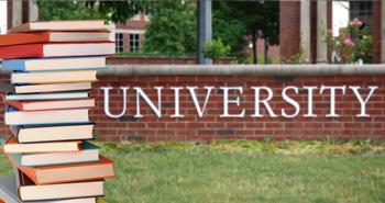 Stack of books in front of brick wall with the word University written on it.